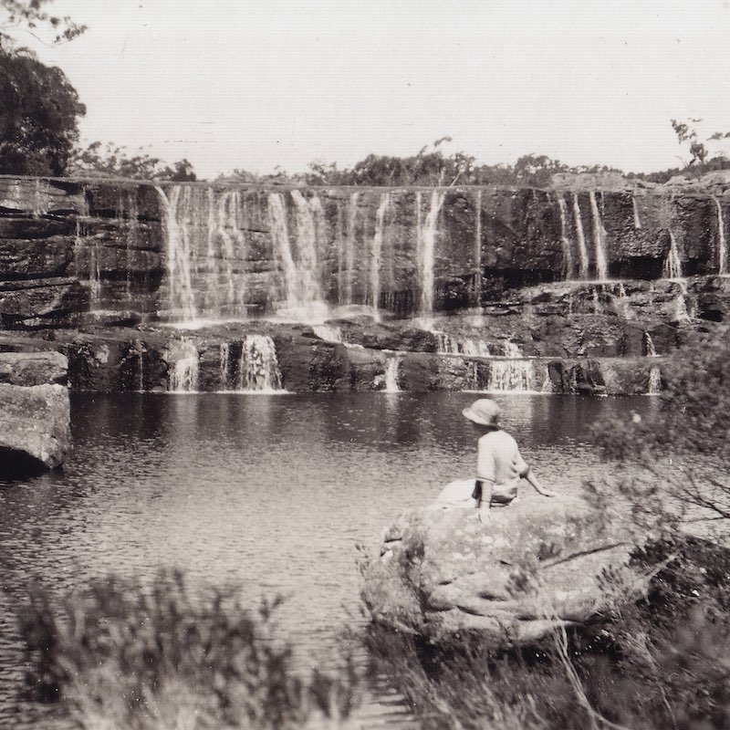 A woman sits on a cliff ledge and quietly enjoys the view of the waterfalls.