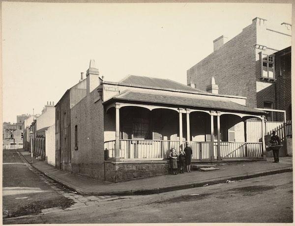 A sepia photograph of a cottage in Francis Street, Darlinghurst. A woman and two children stand by the verandah.