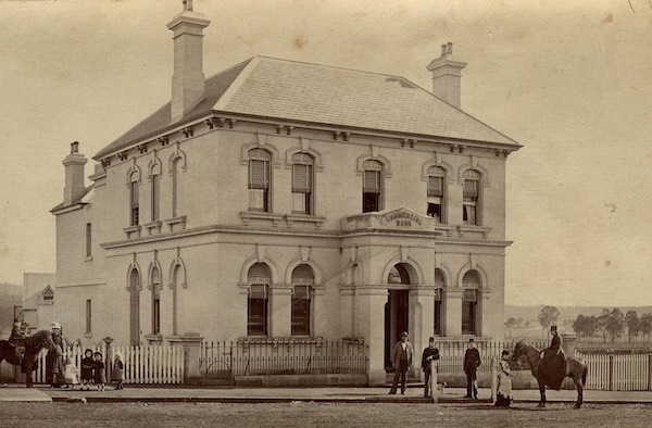 A sepia photograph of the Commercial Bank building. Men and women stand in the foreground.