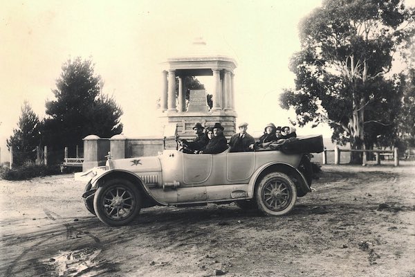A group of seven people sitting in a topless car have their photo taken in front of a monument in Mount York.
