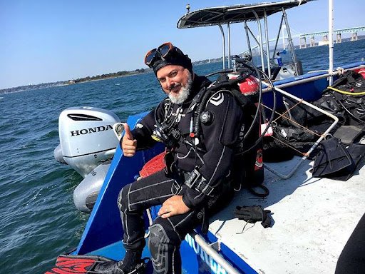 Dr James Hunter gives the thumbs-up to the camera. He is dressed in scuba-diving gear and on a boat.