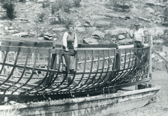 A photograph of a woman and man inside the frame of a boat's hull.