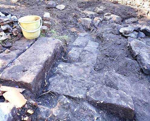 A photograph of exposed stone foundations with a bucket in the corner.