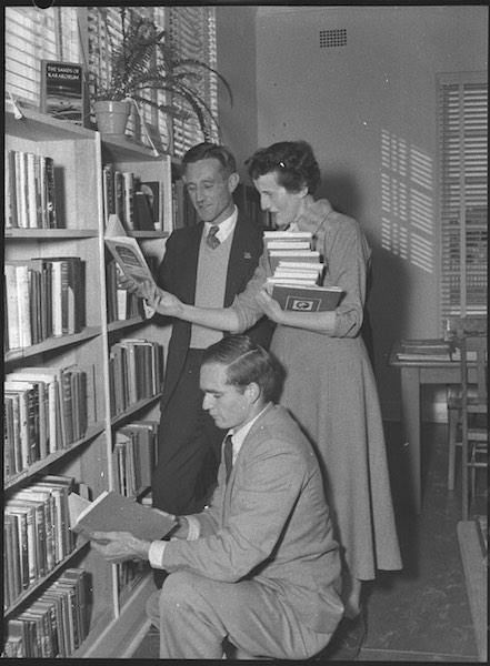 A black and white photograph of a librarian helping people find books.