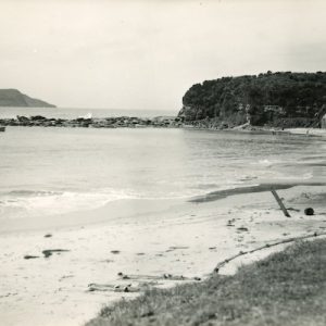 A sepia photograph of Terrigal Beach. Two small boats are moored in the bay, and three sheds are on the beach.